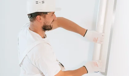 Drywall installer in a hard hat fitting a panel