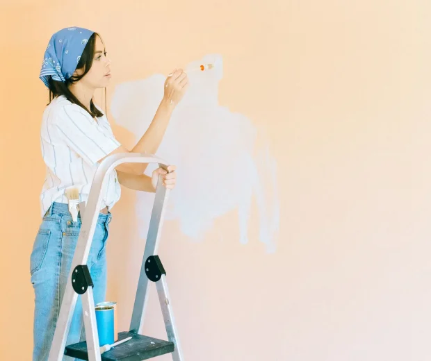 Painter brushing white paint onto a wall from a step ladder