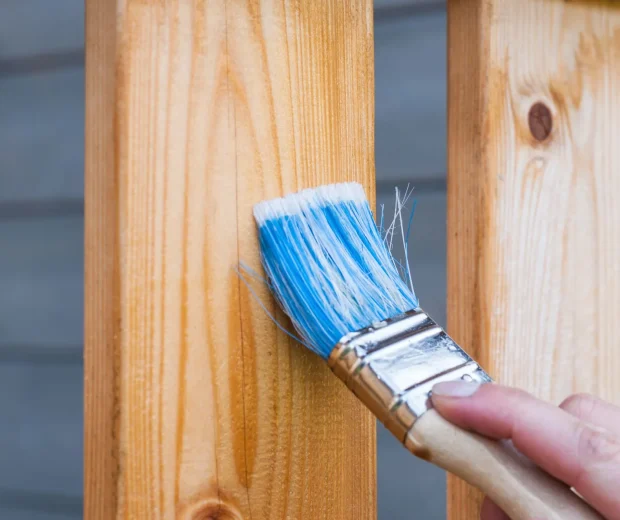 Blue paintbrush applying stain to a wooden railing