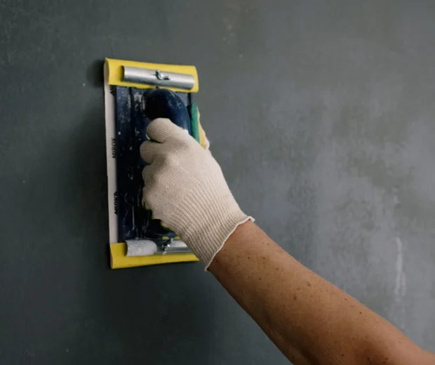 Gloved hand sanding drywall with a sanding block