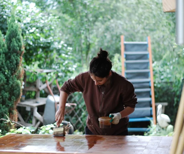 Person brushing wood stain onto a table outdoors
