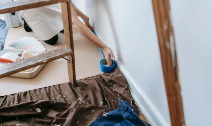 Painter taping baseboard trim over a drop cloth before painting